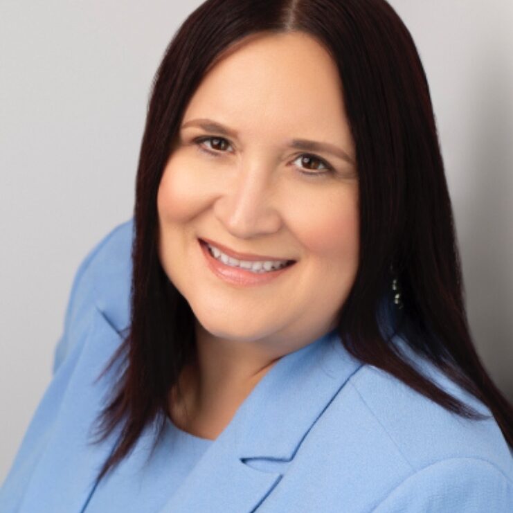 A professional head shot of a woman with dark hair wearing a blue blazer smiling at the camera